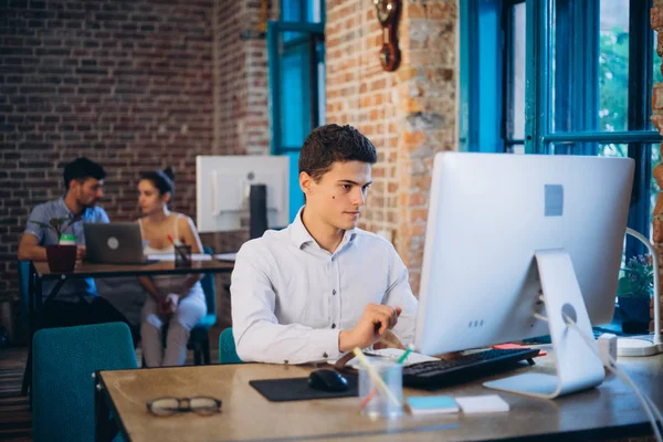 Young bearded businessman in denim shirt is sitting in office at table and is using laptop with charts, graphs and diagrams on screen. Man working.startu