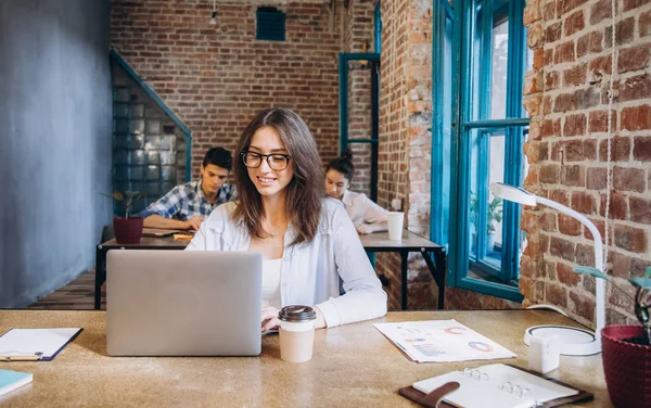 Young bearded businesswoman in denim shirt is sitting in office at table and is using laptop with charts, graphs and diagrams on screen. Man working.startup