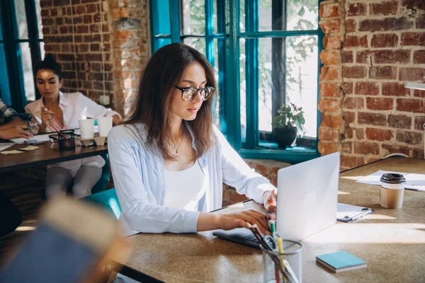 Young bearded businesswoman in denim shirt is sitting in office at table and is using laptop with charts, graphs and diagrams on screen. Man working.startu