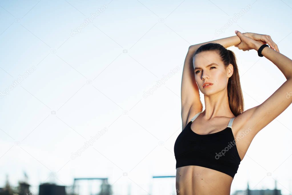 Silhouette of a fitness woman profile stretching at sunrise with the sun in the background. Healthy young woman warming up outdoors. She is stretching her arms and legs.