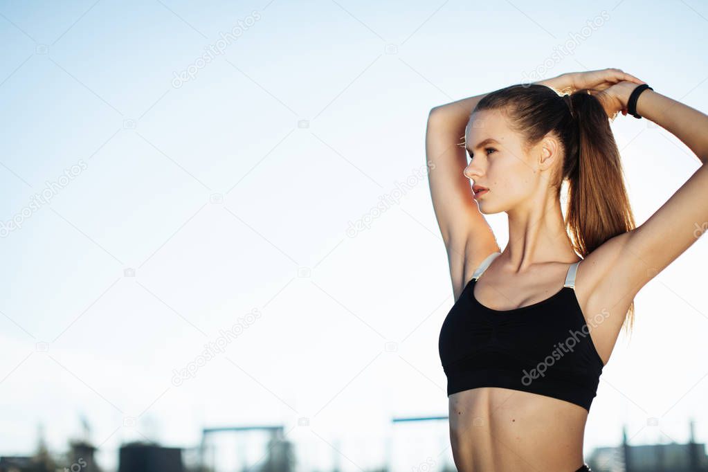Silhouette of a fitness woman profile stretching at sunrise with the sun in the background. Healthy young woman warming up outdoors. She is stretching her arms and legs.