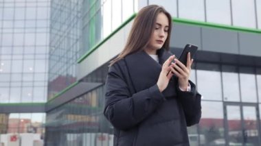 Havaalanı kadınlarda kapısında terminalde bekleyen akıllı telefon. Hava seyahat konsepti ile genç rahat iş kadın konuşmak smartphone, Carry On el Bagaj arabası ile oturuyordu. Güzel genç.