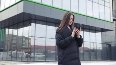 Havaalanı kadınlarda kapısında terminalde bekleyen akıllı telefon. Hava seyahat konsepti ile genç rahat iş kadın konuşmak smartphone, Carry On el Bagaj arabası ile oturuyordu. Güzel genç.