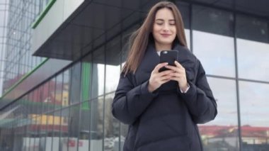 Havaalanı kadınlarda kapısında terminalde bekleyen akıllı telefon. Hava seyahat konsepti ile genç rahat iş kadın konuşmak smartphone, Carry On el Bagaj arabası ile oturuyordu. Güzel genç.