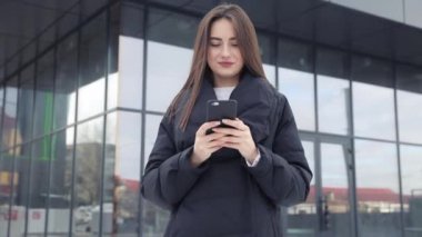 Havaalanı kadınlarda kapısında terminalde bekleyen akıllı telefon. Hava seyahat konsepti ile genç rahat iş kadın konuşmak smartphone, Carry On el Bagaj arabası ile oturuyordu. Güzel genç.