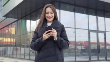 Havaalanı kadınlarda kapısında terminalde bekleyen akıllı telefon. Hava seyahat konsepti ile genç rahat iş kadın konuşmak smartphone, Carry On el Bagaj arabası ile oturuyordu. Güzel genç.