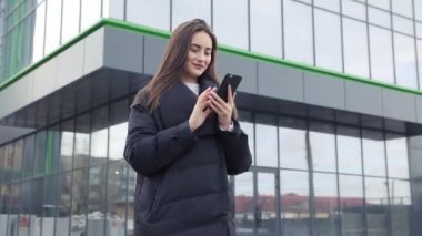 Havaalanı kadınlarda kapısında terminalde bekleyen akıllı telefon. Hava seyahat konsepti ile genç rahat iş kadın konuşmak smartphone, Carry On el Bagaj arabası ile oturuyordu. Güzel genç.