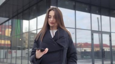 Havaalanı kadınlarda kapısında terminalde bekleyen akıllı telefon. Hava seyahat konsepti ile genç rahat iş kadın konuşmak smartphone, Carry On el Bagaj arabası ile oturuyordu. Güzel genç.
