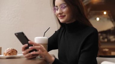Beyaz gömlek giymiş ve modern akıllı telefon, cep telefonu dışında ağır çekim kısa mesaj yazarak profesyonel kadın işveren kullanarak güzel genç kadın