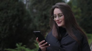 Beyaz gömlek giymiş ve modern akıllı telefon, cep telefonu dışında ağır çekim kısa mesaj yazarak profesyonel kadın işveren kullanarak güzel genç kadın