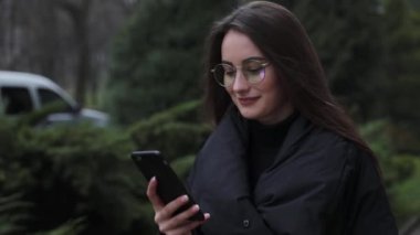 Beyaz gömlek giymiş ve modern akıllı telefon, cep telefonu dışında ağır çekim kısa mesaj yazarak profesyonel kadın işveren kullanarak güzel genç kadın