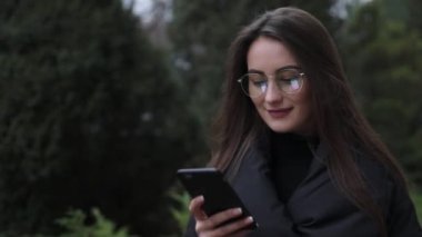 Beyaz gömlek giymiş ve modern akıllı telefon, cep telefonu dışında ağır çekim kısa mesaj yazarak profesyonel kadın işveren kullanarak güzel genç kadın