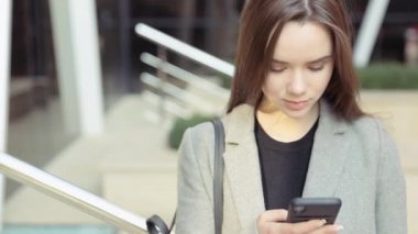 Kendine güvenen genç sıcak, şık bir pembe ceketli sarışın kız Havaalanı terminal tarafından yürür ve cep telefonunu kullanır gülümseyerek mutlu bir şekilde metin mesajları için etrafına bakıyor. Şık kıyafet, modern kadın.
