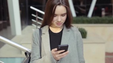 Kendine güvenen genç sıcak, şık bir pembe ceketli sarışın kız Havaalanı terminal tarafından yürür ve cep telefonunu kullanır gülümseyerek mutlu bir şekilde metin mesajları için etrafına bakıyor. Şık kıyafet, modern kadın.