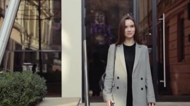 Kendine güvenen genç sıcak, şık bir pembe ceketli sarışın kız Havaalanı terminal tarafından yürür ve cep telefonunu kullanır gülümseyerek mutlu bir şekilde metin mesajları için etrafına bakıyor. Şık kıyafet, modern kadın.