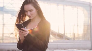 Havaalanı kadınlarda kapısında terminalde bekleyen akıllı telefon. Hava seyahat konsepti ile genç rahat iş kadın konuşmak smartphone, Carry On el Bagaj arabası ile oturuyordu. Güzel genç.
