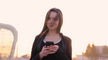 Havaalanı kadınlarda kapısında terminalde bekleyen akıllı telefon. Hava seyahat konsepti ile genç rahat iş kadın konuşmak smartphone, Carry On el Bagaj arabası ile oturuyordu. Güzel genç.