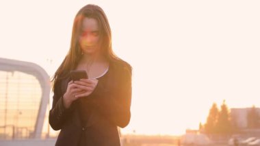 Havaalanı kadınlarda kapısında terminalde bekleyen akıllı telefon. Hava seyahat konsepti ile genç rahat iş kadın konuşmak smartphone, Carry On el Bagaj arabası ile oturuyordu. Güzel genç.