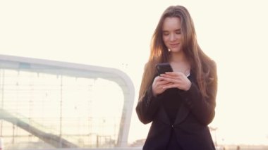 Havaalanı kadınlarda kapısında terminalde bekleyen akıllı telefon. Hava seyahat konsepti ile genç rahat iş kadın konuşmak smartphone, Carry On el Bagaj arabası ile oturuyordu. Güzel genç.