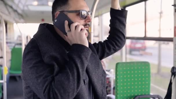 スマートフォンで話す電車の中で魅力的な男の肖像笑顔幸せな男の手インターネット技術携帯電話市の携帯電話のスマートフォントラム女性輸送若い遅い動き — ストック動画