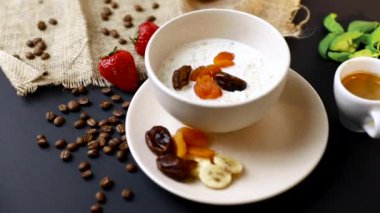 Lezzetli kahvaltı. Siyah masa üzerinde yulaf, fındık ve kurutulmuş meyve ile müsli bir kase üst görünümü. Yavaş mo
