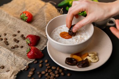 Lezzetli kahvaltı. Siyah masa üzerinde yulaf, fındık ve kurutulmuş meyve ile müsli bir kase üst görünümü. Yavaş m