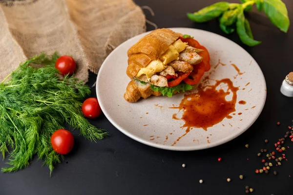 Tasty breakfast. Appetizing croissant with meat and, cheese and tomatoes. black background with vegetables. Slow-m