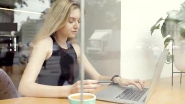 Çekici genç kadın kafede dizüstü bilgisayara bir kredi kartı numarası girerken online alışveriş. Içinde