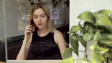 Dizüstü bilgisayar kullanarak masada oturan, çağrıya cevap veren, telefonda konuşan, cep telefonuyla konuşan genç, kafede bilgisayarla çalışırken cep telefonundan keyifli sohbet ler veren genç,