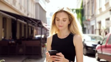 Mutlu Gülümseyen Çekici Kadın Sokakta Yürürken. İlgiyle Akıllı Telefonunda Yazarak. Akşam Yürüyüşü'nün tadını çıkarıyorum. Arka Planda Kalabalık Şehir.