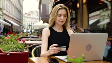 Çekici genç kadın kafede dizüstü bilgisayara bir kredi kartı numarası girerken online alışveriş. Içinde
