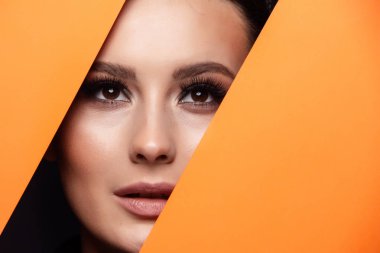 Kahverengi gölgeler ve etkileyici kaşları ile güzel köri parlak güzel gözleri olan bir kız renkli kağıt deliğine bakar. Moda, güzellik, makyaj, kozmetik, makyaj sanatçısı, güzellik salonu, kartvizit.