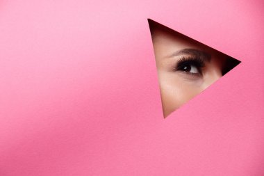 Kahverengi gölgeler ve etkileyici kaşları ile güzel köri parlak güzel gözleri olan bir kız renkli kağıt deliğine bakar. Moda, güzellik, makyaj, kozmetik, makyaj sanatçısı, güzellik salonu, kartvizit.