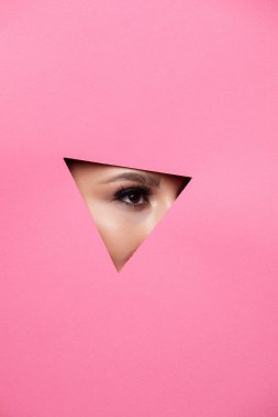 Kahverengi gölgeler ve etkileyici kaşları ile güzel köri parlak güzel gözleri olan bir kız renkli kağıt deliğine bakar. Moda, güzellik, makyaj, kozmetik, makyaj sanatçısı, güzellik salonu, kartvizit.