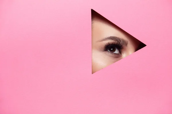 A girl with beautiful curry bright beautiful eyes with brown shadows and expressive eyebrows looks into the hole of colored paper.Fashion, beauty, make-up, cosmetics, make-up artist, beauty salon,business card.