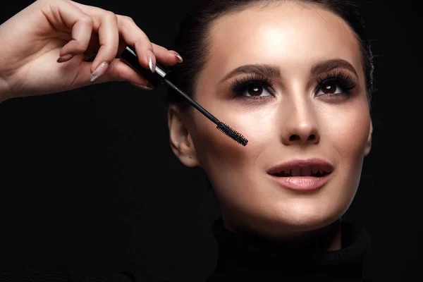 Beauty Cosmetics.Woman applying black mascara on eyelashes with makeup brush. photos of appealing brunette girl on black background.High Resolution