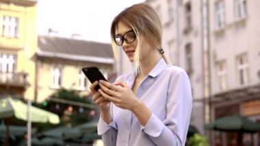 Mavi gömlek giyen ve modern akıllı telefon kullanarak güzel genç kadın, profesyonel kadın işveren dışında cep telefonu metin mesajı yazarak, yavaş hareket