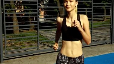 Sokakta çalışan, müzik dinlemek güzel kadın. Güzel kız Runner parlak spor giyim, spor aygıtları giyiyor: Fitness izci, kulaklık ve açık havada koşu kol bandı. Yüksek çözünürlük