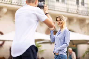 Turist çift. Kamera çekim kadının sokakta olan adam. Gülümseyen genç Çift seyahat ve fotoğrafları açık havada yapma şık giysiler içinde aşık. İnsanlar seyahat hafta sonu. Yüksek çözünürlük.