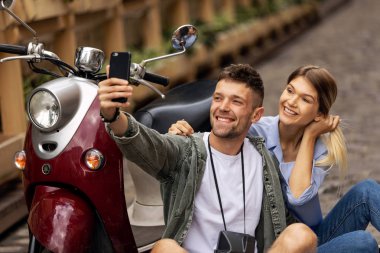 Scooter'daki mutlu çift, dışarıda akıllı telefonda selfie fotoğrafı çekiyor. İnsanlar hafta sonu seyahat. Yüksek Çözünürlük.