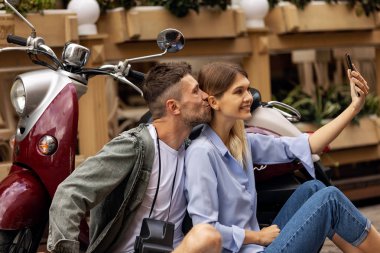 Scooter'daki mutlu çift, dışarıda akıllı telefonda selfie fotoğrafı çekiyor. İnsanlar hafta sonu seyahat. Yüksek Çözünürlük.