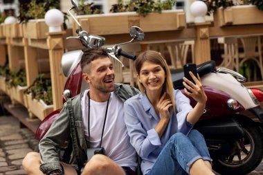 Scooter'daki mutlu çift, dışarıda akıllı telefonda selfie fotoğrafı çekiyor. İnsanlar hafta sonu seyahat. Yüksek Çözünürlük.