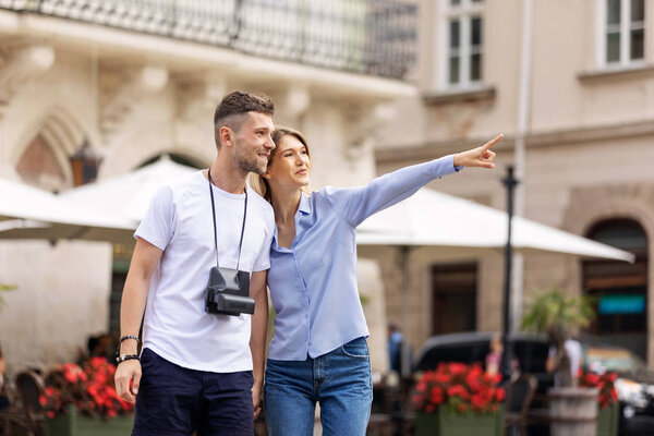 Travel. Tourist Couple Traveling, Walking On Street. Portrait Of Beautiful Young Woman And Handsome Man In Stylish Clothes Sightseeing City Attractions, Looking At Architecture. High Resolution.