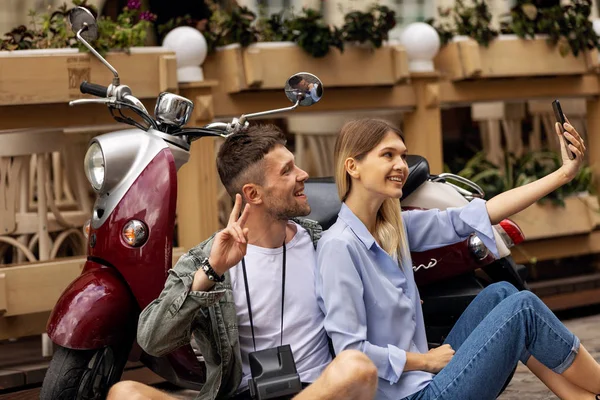 Happy couple on scooter making selfie photo on smartphone outdoors. People Travel On Weekend. High Resolution.