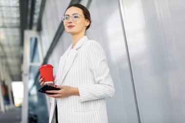 Sabah erken işe gitmeden gitmek başarılı iş kadını modern smartphone kullanarak ve kahve içme takım giyen kırpılmış görüntü