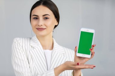 Beyaz kazak gülümseyen genç iş kadını yeşil ekranlı akıllı telefon gösteren, uygulama
