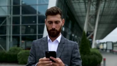 Akıllı telefon kullanan ve havaalanında gülümseyen işadamı. Havaalanında cep telefonu ile genç iş yöneticisi.