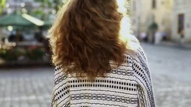 Güzel, şık görünümlü kıvırcık bir kadın sokakta rahatça yürür, son moda gül güneş gözlüğüne dokunur, parlak güneş ışığına dokunur. Yaşam sevinci, aktif yaşam tarzı, moda blogcusu, podyum