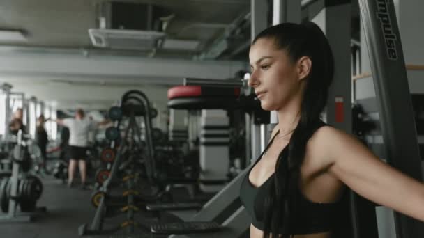 Självsäker fitness flicka med mörkt hår i sportkläder med hjälp av gym simulator för att pumpa muskler på under regelbunden träning. Begreppet styrka, självdisciplin och hälsosam livsstil. — Stockvideo