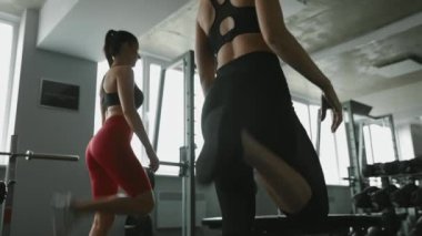 Spor sutyenli ve taytlı genç kızların spor salonundaki antrenmandan önce bacaklarını ısıtmasının düşük açılı görüntüsü. Motivasyon, destek ve aktif yaşam tarzı kavramı.